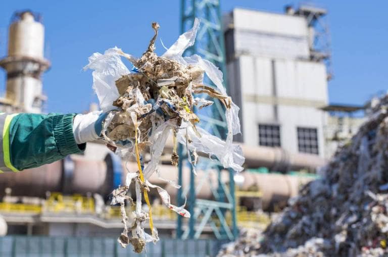 person with glove holding pile of trash at waste to energy treatment plant