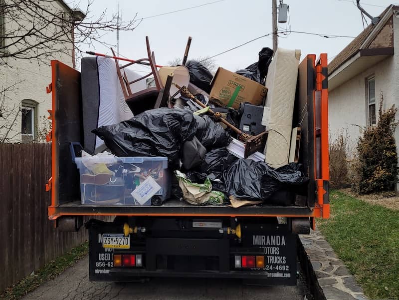 fully loaded junk removal truck picking up trash from suburban home for waste to energy disposal