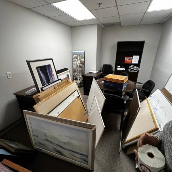 cluttered office storage closet with old white boards picture frames and boxes